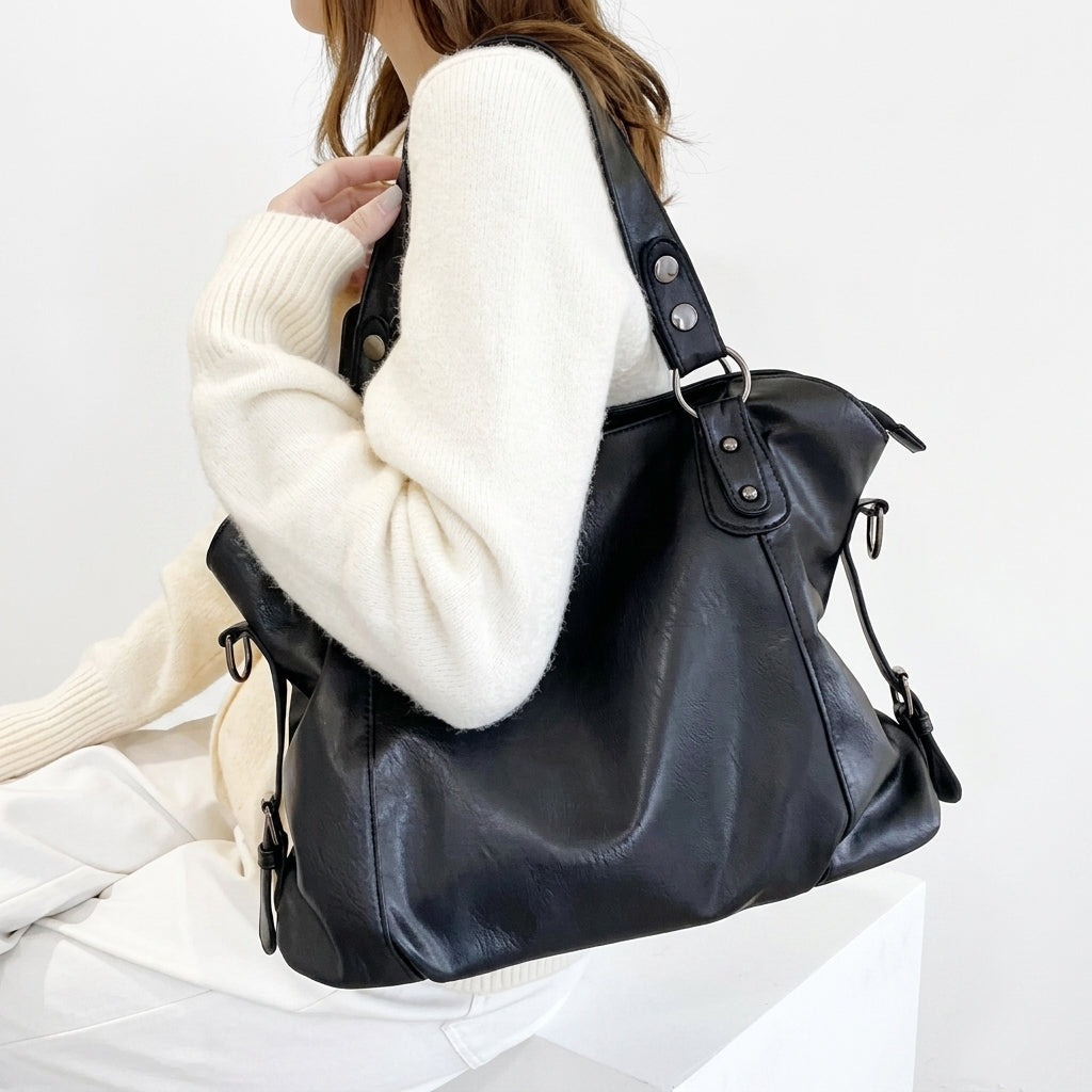 Assise en pull blanc, une jeune femme garde le hobo noir à l'épaule, matière brillante et plissée