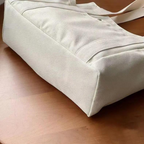 Base plate du sac écru posé sur un parquet, coutures renforcées et poche latérale visibles