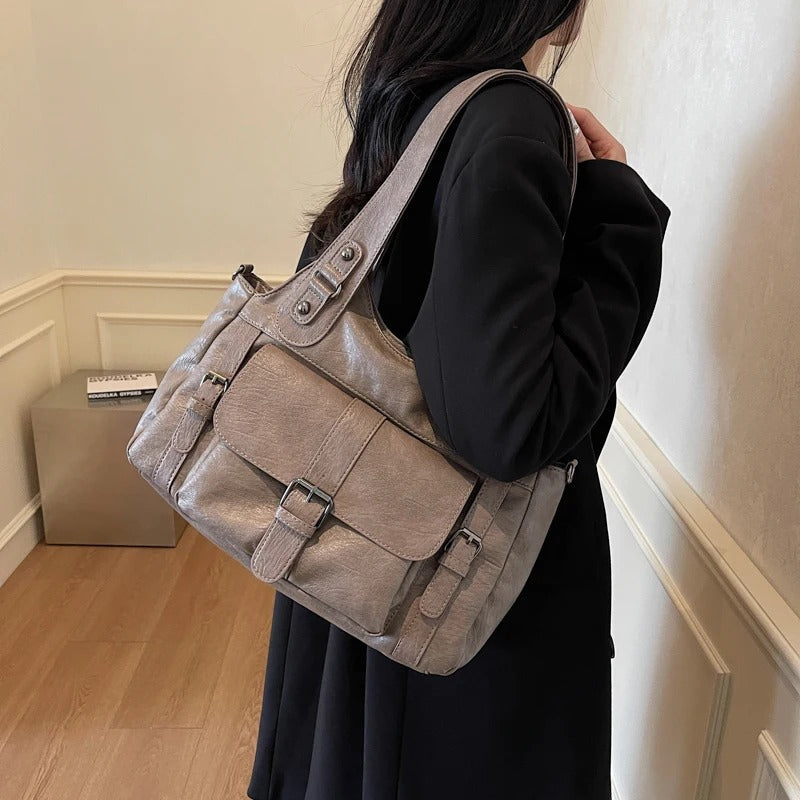 Épaulé le long d'un manteau noir, le sac gris taupe montre son rabat bouclé et son anse plate