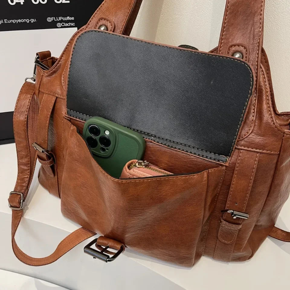 Détail de la poche frontale ouverte du sac cognac, un téléphone et une pochette glissés dedans