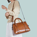Sangle en croisé sur une tenue beige et blanche, le sac cognac repose contre la hanche