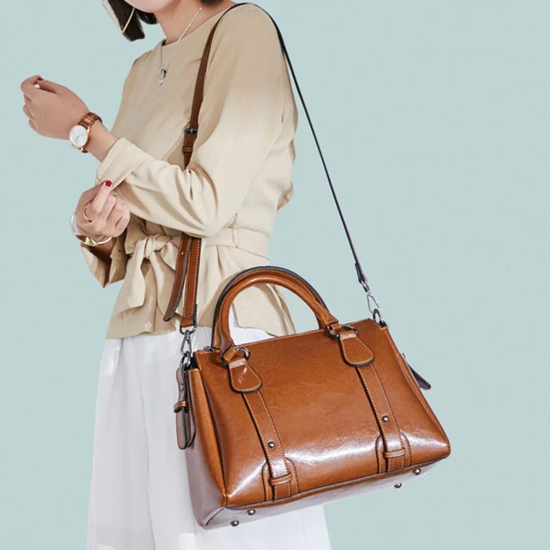 Sangle en croisé sur une tenue beige et blanche, le sac cognac repose contre la hanche
