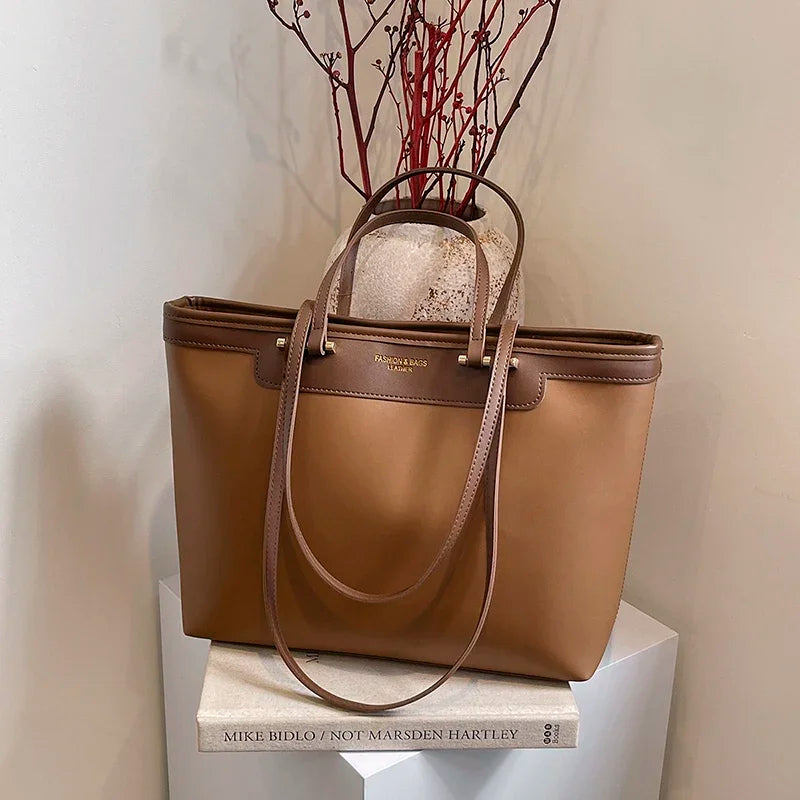 Camel lumineux, ce cabas est présenté sur un socle blanc devant un mur beige et un vase