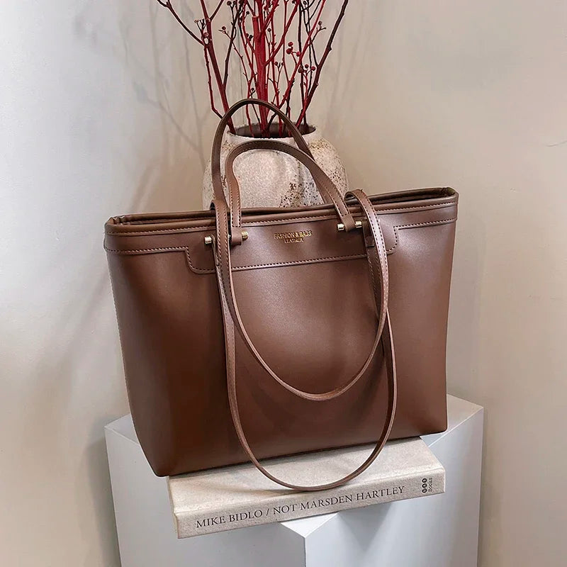 Sur un socle blanc devant un vase de branches rouges, le cabas chocolat montre son flanc