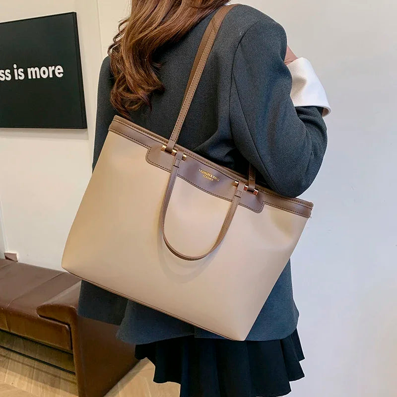 Porté à l'épaule de dos, le cabas écru repose contre une veste grise et une jupe plissée