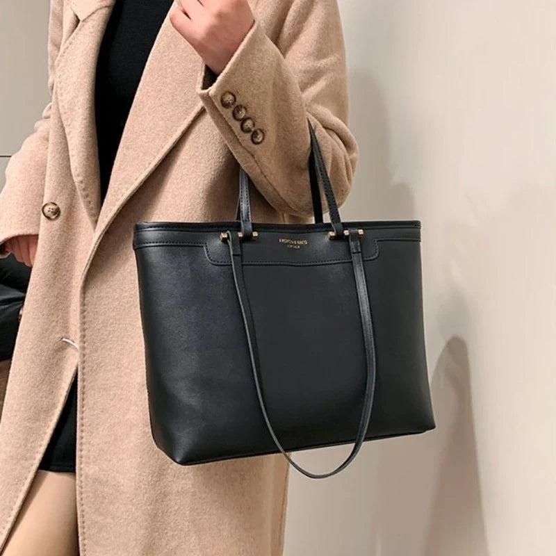 Manteau camel ouvert et cabas noir tenu à la main, la longue anse retombe le long du sac