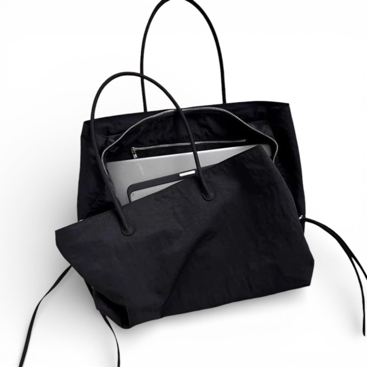 Ordinateur portable glissé dans le cabas noir ouvert, glissière et poche interne visibles