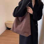 Suédine vieux rose portée au creux du bras, grand sac souple sur un manteau bleu marine