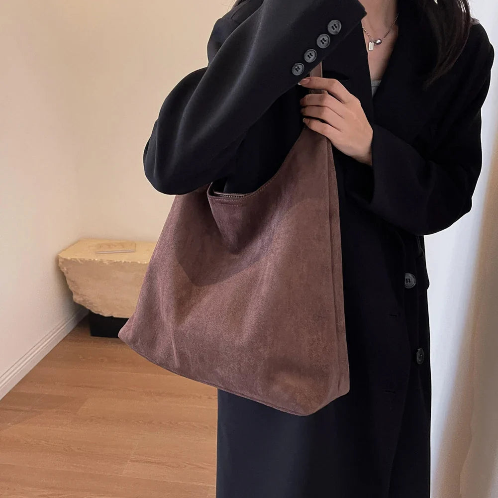 Suédine vieux rose portée au creux du bras, grand sac souple sur un manteau bleu marine