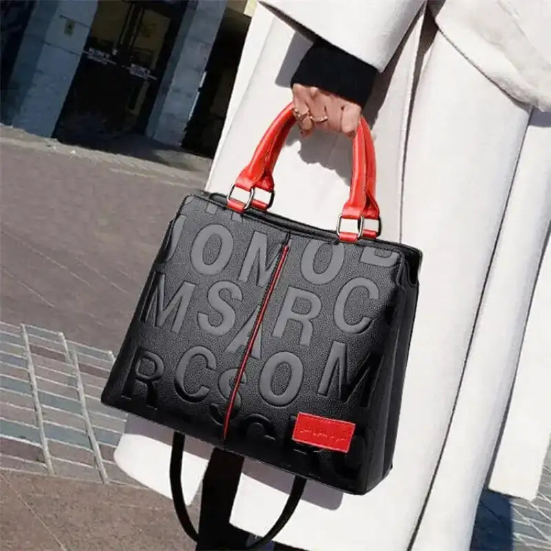 Tenu à la main par son anse rouge dans la rue, le sac noir montre ses lettres en relief