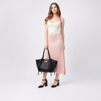 Silhouette en jupe rose satinée tenant le cabas noir à la main, plan en pied sur fond gris