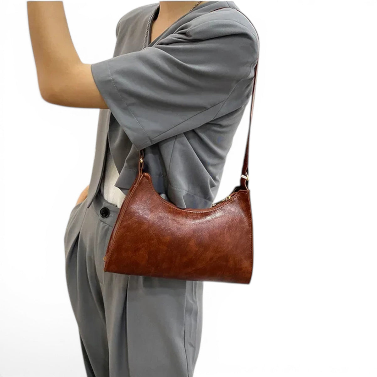 Glissé sous le bras sur un ensemble gris, le hobo cognac suit la ligne du corps, zip apparent