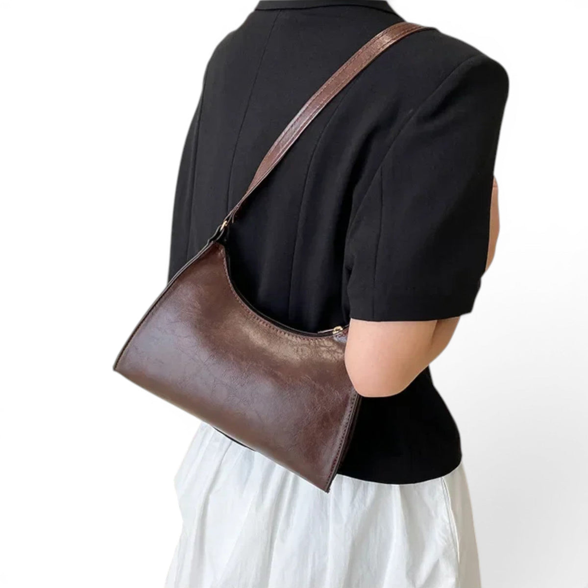 De dos, sac marron porté à l'épaule sur une veste noire, sangle plate posée sur l'omoplate