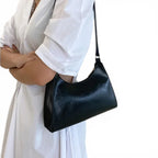 Sous le bras d'une femme en chemise blanche, le petit sac noir épouse la hanche, anse à l'épaule