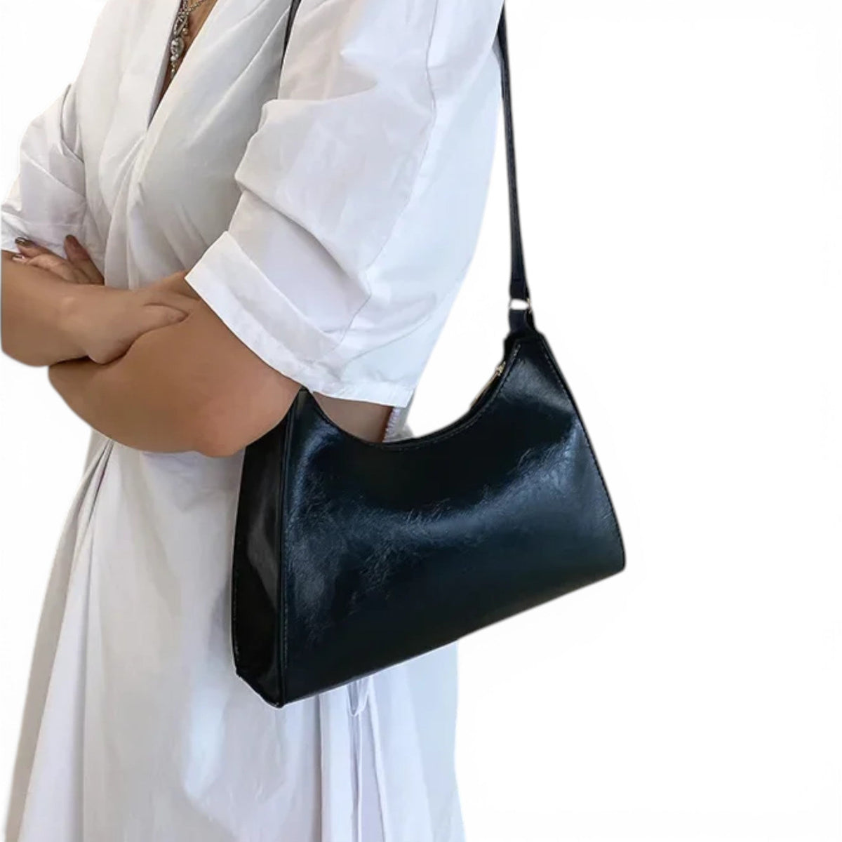 Sous le bras d'une femme en chemise blanche, le petit sac noir épouse la hanche, anse à l'épaule