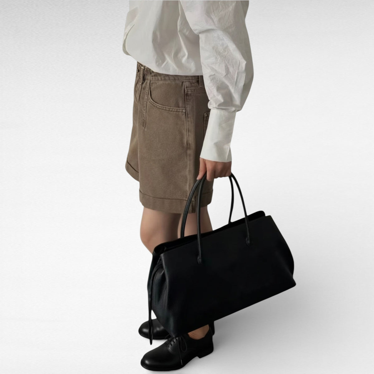 Cabas noir tenu à la main le long d'un short marron, format allongé posé contre la jambe