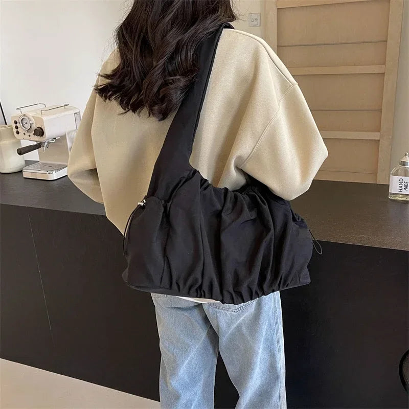 Sur un sweat beige, le hobo noir en nylon froncé se porte à l'épaule, corps souple et arrondi