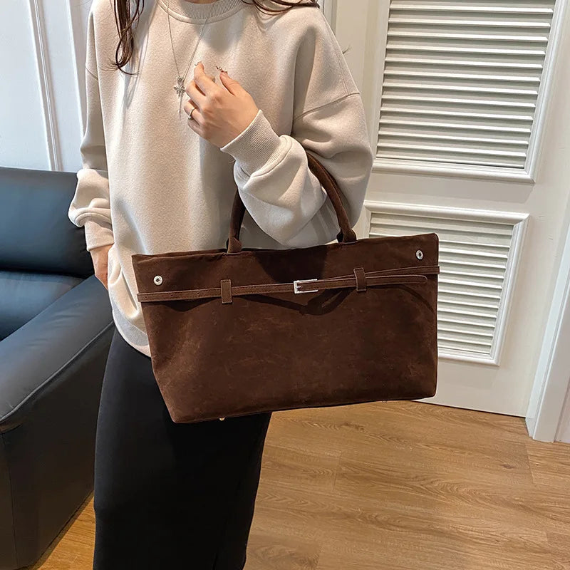 Sac brun chocolat calé sur l'avant-bras, façade tendue et boucle argentée centrée sur la ceinture