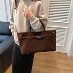 Sac brun chocolat calé sur l'avant-bras, façade tendue et boucle argentée centrée sur la ceinture
