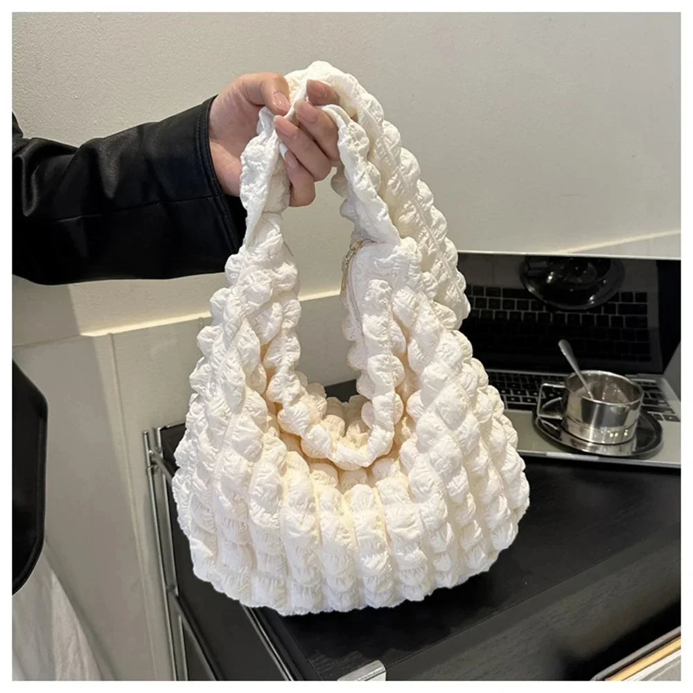 Attrapé par son anse au-dessus d'un plan de travail sombre, le sac ivoire montre son relief bullé