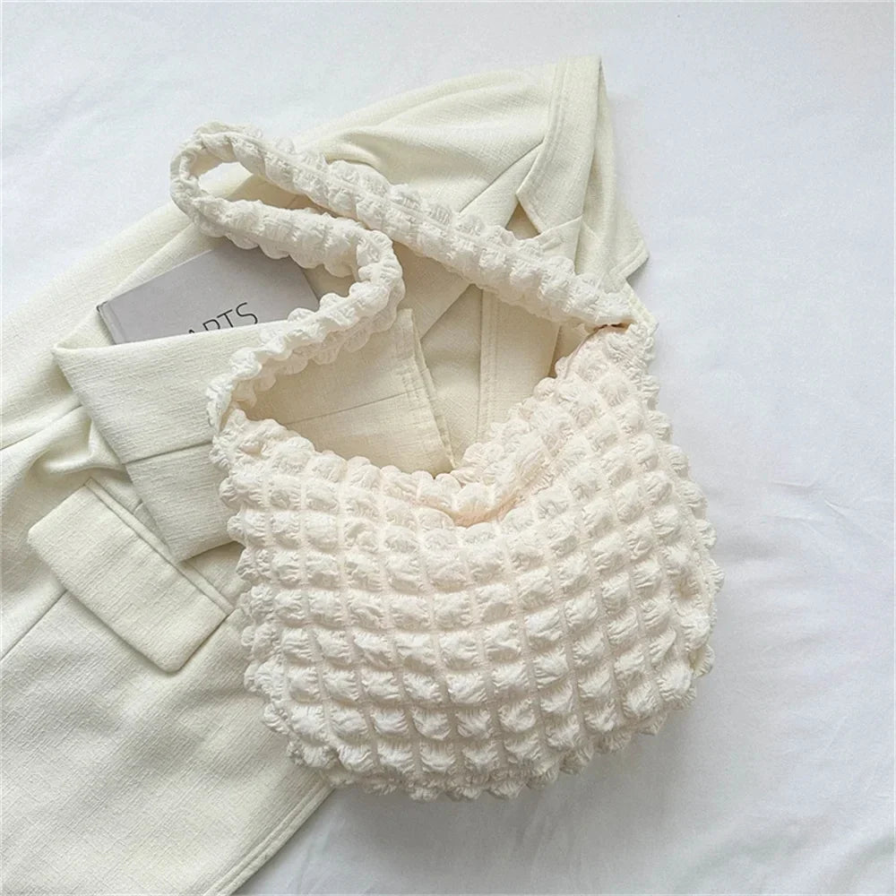 Écru légèrement crème, le hobo gaufré repose sur un blazer clair, son anse large formant une boucle