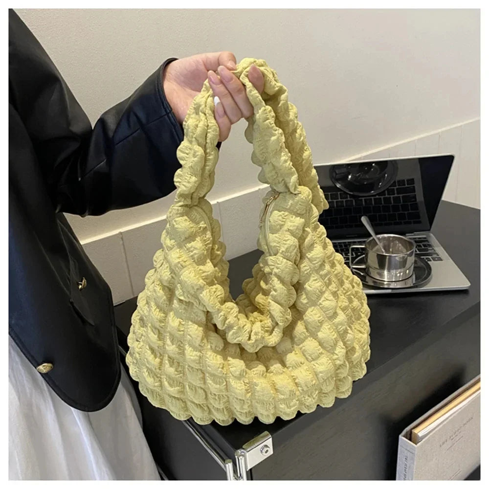 Saisi à la main près d'un ordinateur, le sac jaune pâle laisse voir sa texture bullée et souple