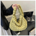 Saisi à la main près d'un ordinateur, le sac jaune pâle laisse voir sa texture bullée et souple