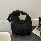 Devant un ordinateur portable, le sac noir texturé attend sur un bureau sombre, anse rabattue
