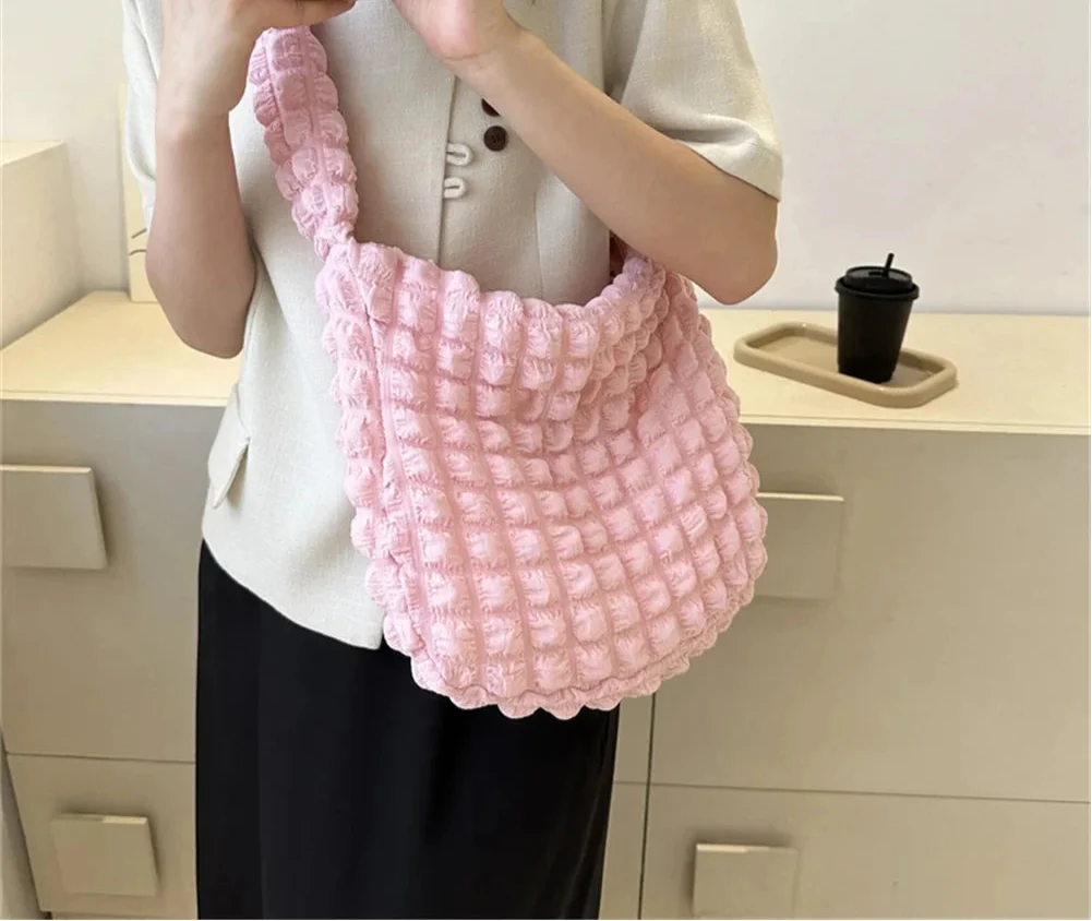 Porté à l'épaule devant un haut écru et un pantalon noir, le hobo rose pâle gonfle sa texture