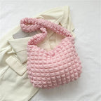Nuance rose pâle pour le même sac gaufré, posé sur une veste crème avec son anse repliée