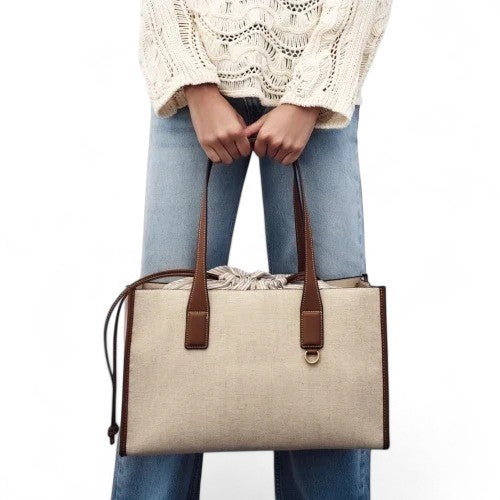 Empoigné à deux mains devant un jean droit, le cabas beige lin contraste avec ses anses caramel