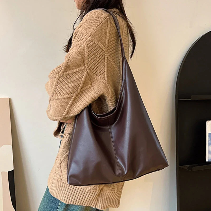Épaule chargée du hobo brun café, porté par-dessus un gilet beige, le sac descend sur la hanche