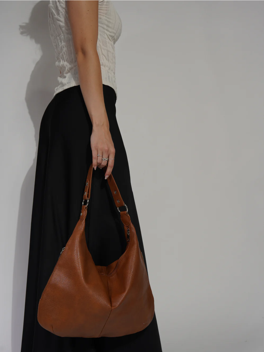 À bout de bras le long d'une jupe noire, le sac caramel se balance, anse repliée en deux