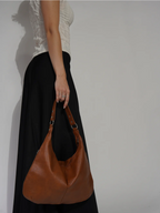 À bout de bras le long d'une jupe noire, le sac caramel se balance, anse repliée en deux