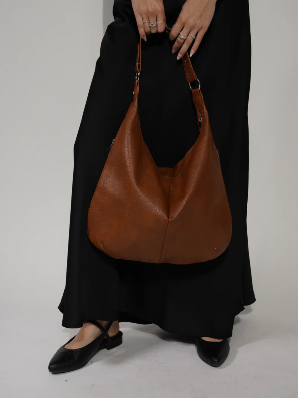 Tenu par la sangle devant un pantalon noir fluide, le sac caramel descend jusqu'à la cuisse