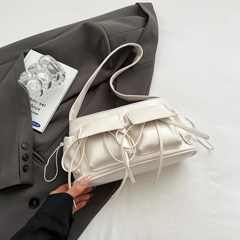 Blanc écru légèrement nacré, le sac baguette posé à plat, doubles poches et liens noués visibles
