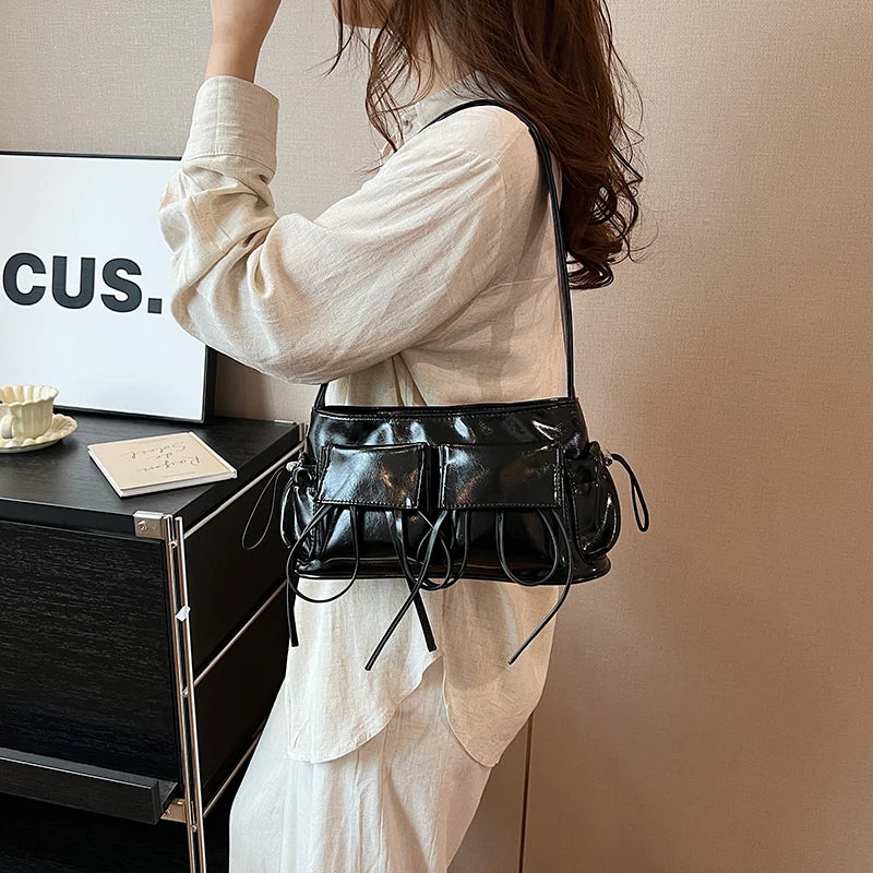 Porté à l'épaule sur une chemise crème, le sac baguette noir verni vient se poser sur la hanche