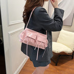 Porté à l'épaule sur une veste noire, le petit sac rose accompagne une jupe plissée sombre