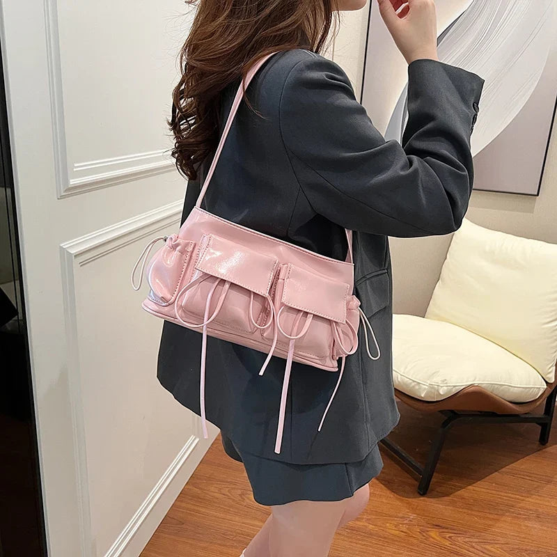 Porté à l'épaule sur une veste noire, le petit sac rose accompagne une jupe plissée sombre