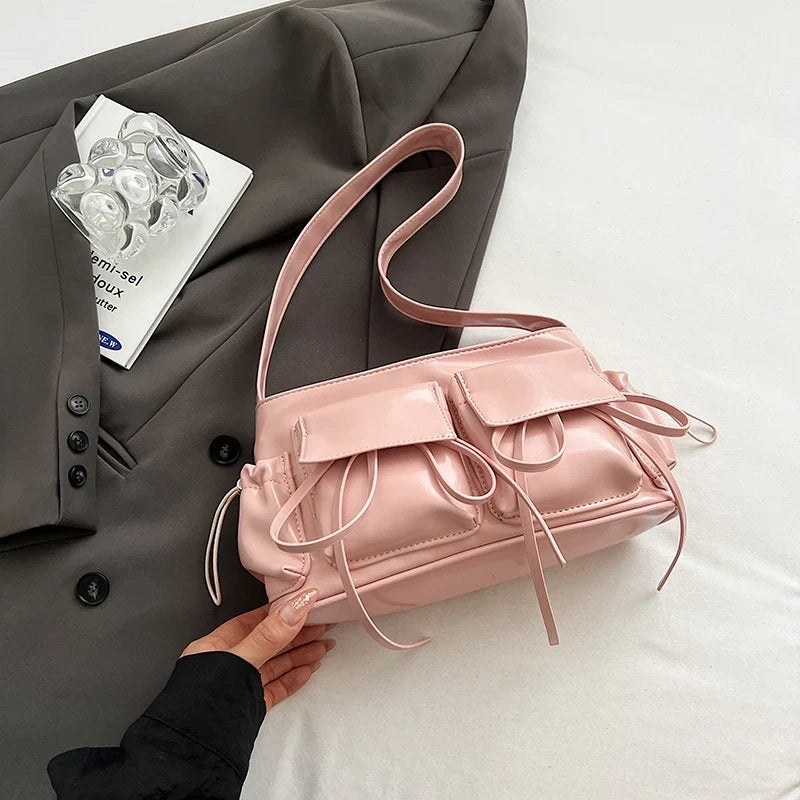 Rose pâle satiné, le sac baguette est présenté à plat sur une veste grise, anse repliée dessus