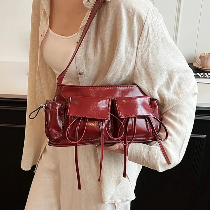 Porté en croisé sur un gilet beige, le sac bordeaux souligne la taille, liens retombant devant