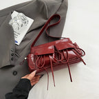 Rouge bordeaux lustré, le sac repose à plat sur un tissu gris, cordons étalés devant lui