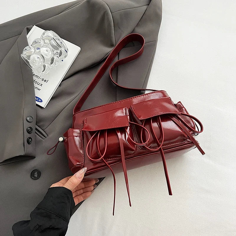 Rouge bordeaux lustré, le sac repose à plat sur un tissu gris, cordons étalés devant lui