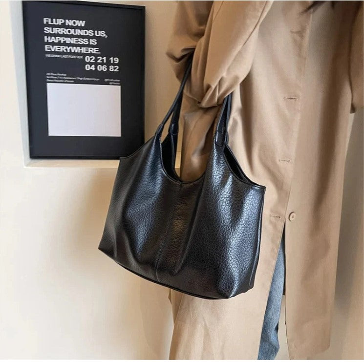 Anses réunies sur l'épaule d'un trench camel, le sac noir descend le long de la hanche du modèle