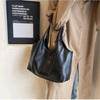 Anses réunies sur l'épaule d'un trench camel, le sac noir descend le long de la hanche du modèle