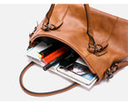 Contenu du sac ouvert : cahiers, stylos et tablette glissés dans le grand compartiment caramel