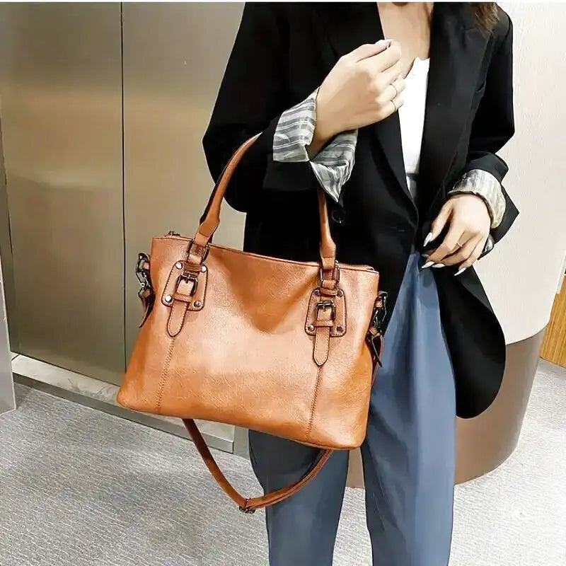 Le cabas caramel porté au bras, sur un blazer noir et un pantalon bleu, tombe le long du corps