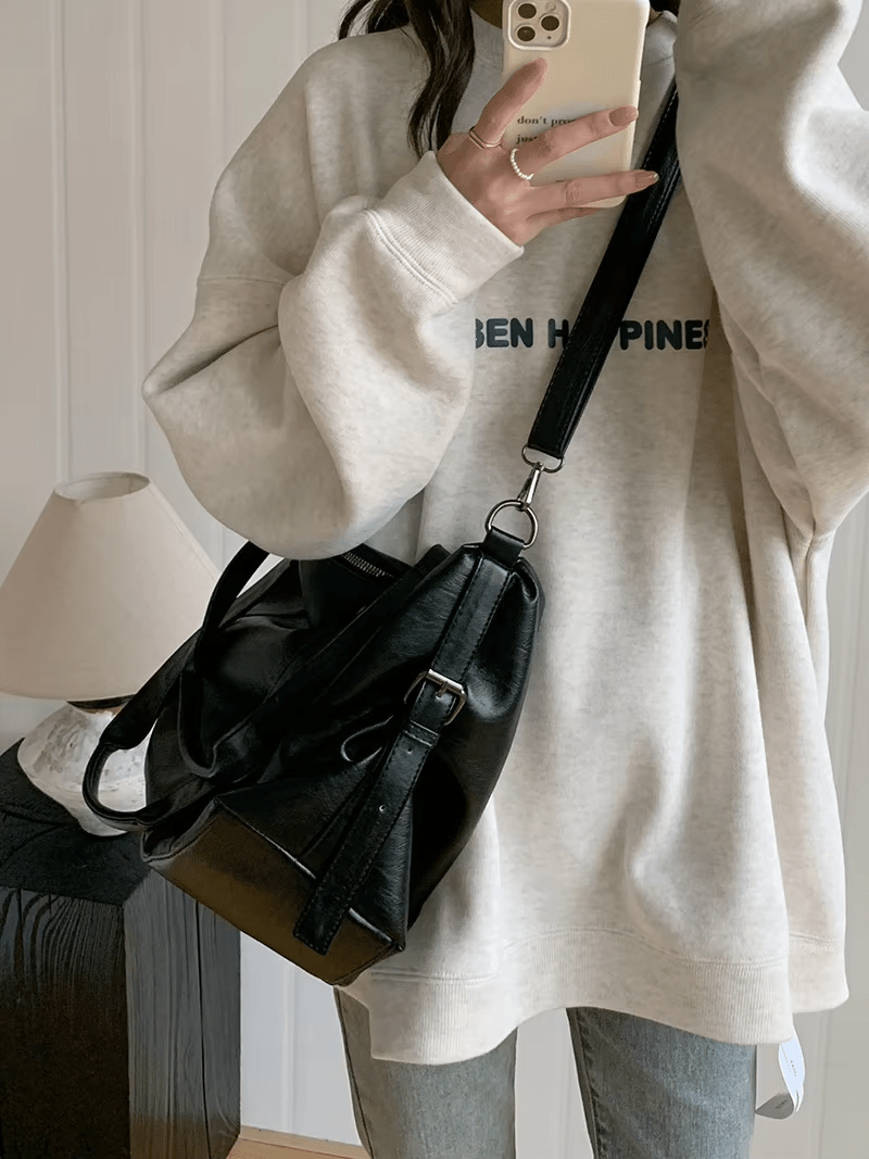 Porté en croisé sur un sweat écru, le sac noir repose sur la hanche, sangle large en travers du buste