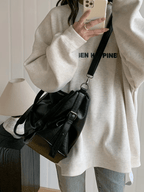 Porté en croisé sur un sweat écru, le sac noir repose sur la hanche, sangle large en travers du buste