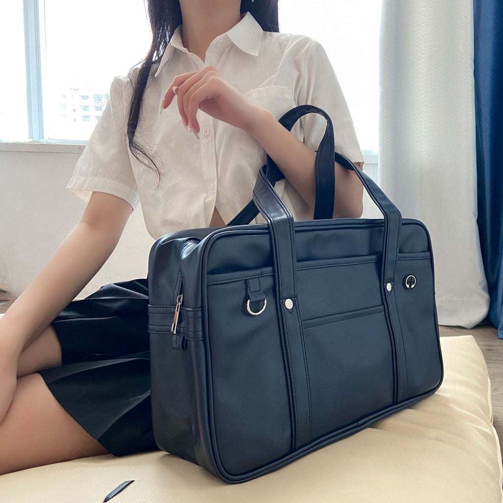 Posé sur un lit clair, le sac bleu marine côtoie une chemise blanche et une jupe plissée noire